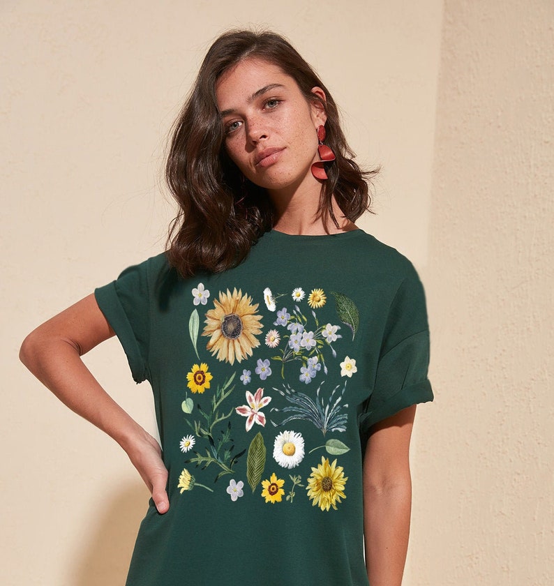 May include: A dark green t-shirt with a floral print featuring sunflowers, daisies, and other wildflowers in shades of yellow, white, and pink.
