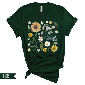May include: A dark green t-shirt with a floral print featuring sunflowers, daisies, and other wildflowers. The print is centered on the shirt and covers most of the front.