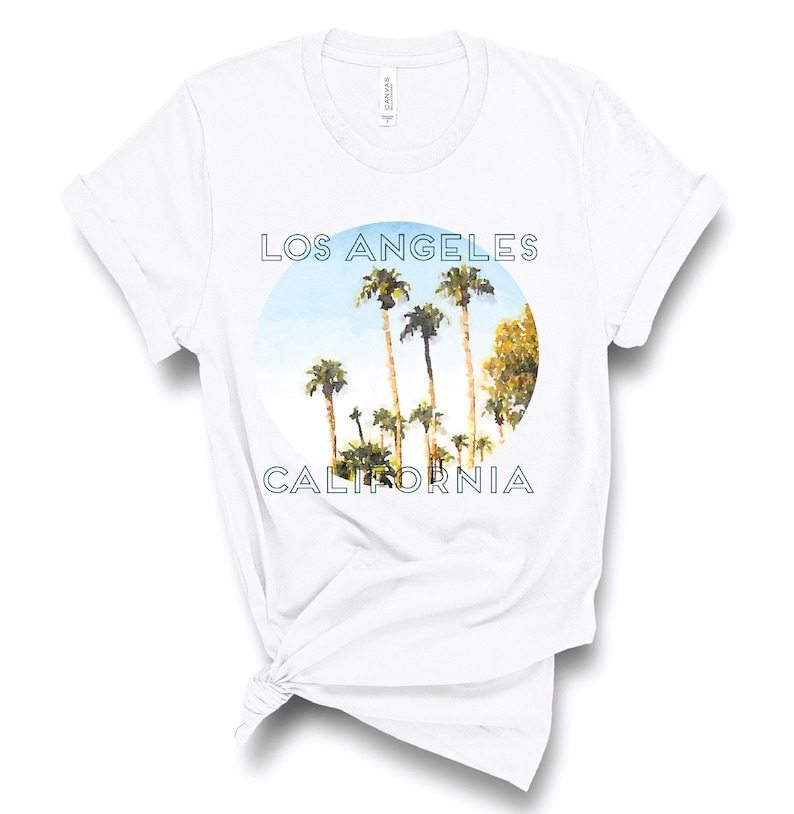 May include: White t-shirt with a graphic print of palm trees in a circle with the text "Los Angeles California" in blue.