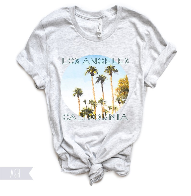 May include: A heather grey t-shirt with a circular graphic of palm trees against a blue sky. The graphic says "Los Angeles California" in a teal font.