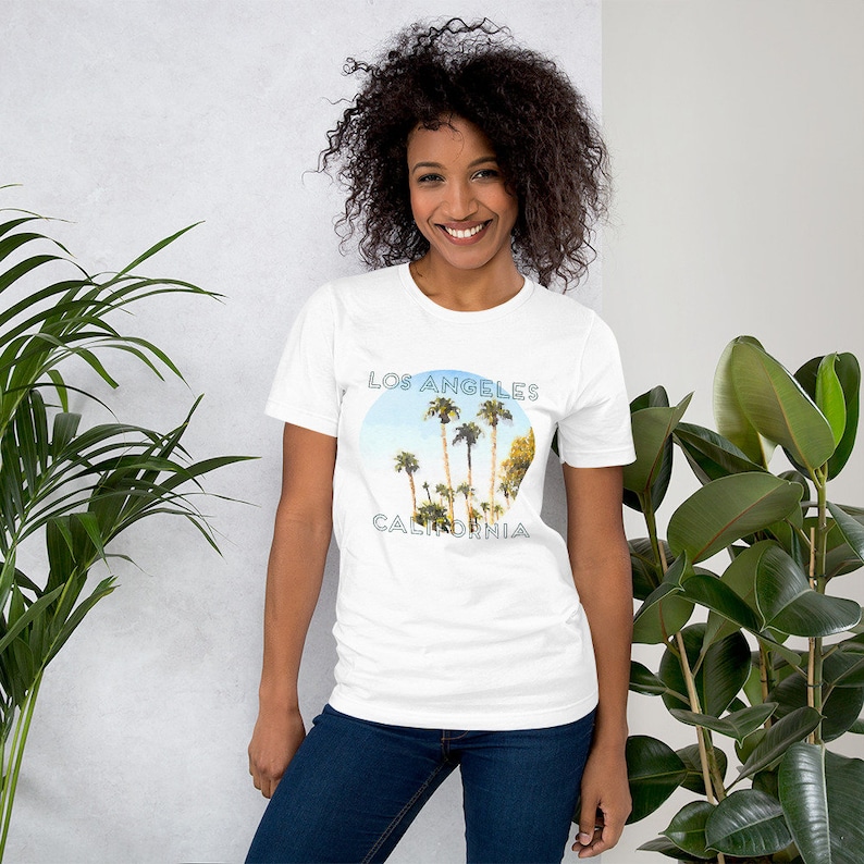 May include: White t-shirt featuring a graphic of palm trees and the text "Los Angeles California" in a blue circle.
