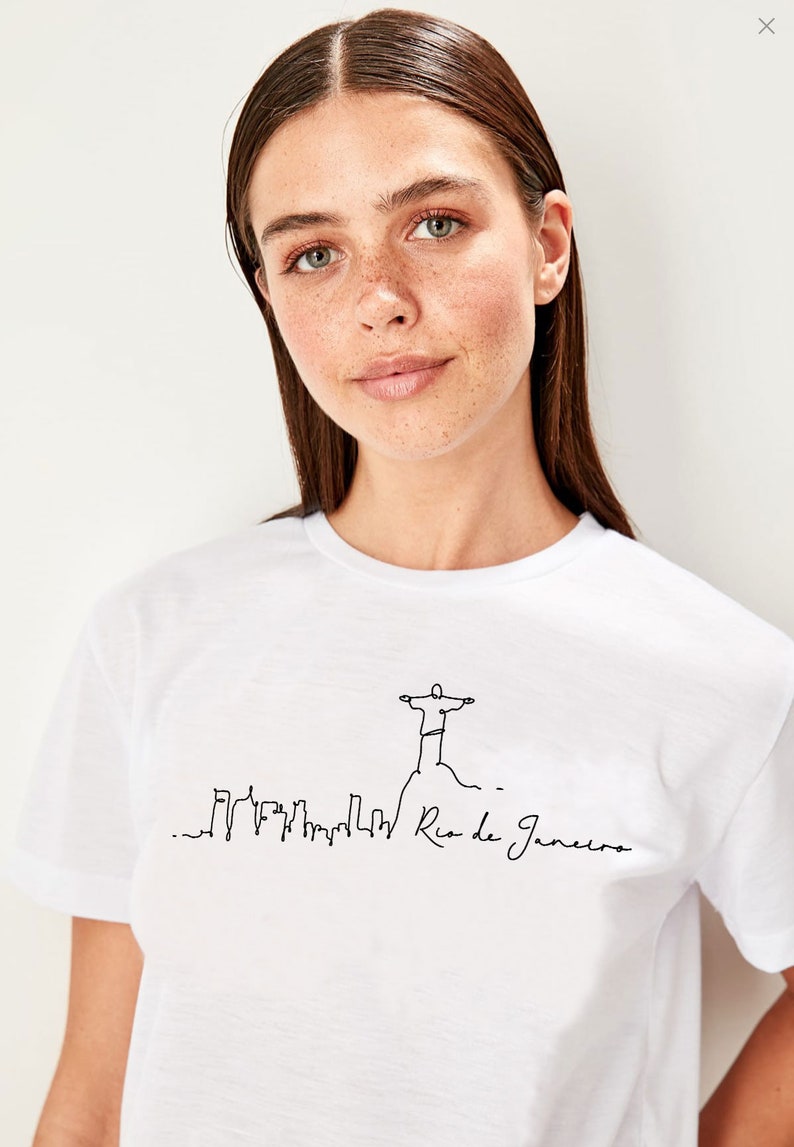 May include: White t-shirt with a black line drawing of the Christ the Redeemer statue in Rio de Janeiro, Brazil. The drawing also includes a skyline of the city and the text "Rio de Janeiro".
