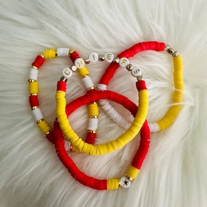 May include: Three colorful bracelets with white and yellow beads, and red and yellow beads. The bracelets have gold beads with white letters spelling out "CHIEFS" on them. One bracelet has a gold star bead.