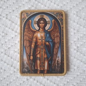 Op de afbeelding: Rechthoekige religieuze icoon met een gedetailleerde afbeelding van een engel met grote vleugels, gekleed in gouden en blauwe gewaden. Het icoon heeft een gouden rand en een blauwe hemel als achtergrond.