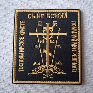 May include: A black embroidered patch with gold thread. The patch features a cross with the words "Сыне Божий" (Son of God) at the top and "Господи Иисусе Христе" (Lord Jesus Christ) on the left and "Помилуй мя грешного" (Have mercy on me, a sinner) on the right.