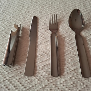 以下が含まれることがあります： ステンレス製のカトラリーセット。栓抜き、ナイフ、フォーク、スプーンが含まれています。これらの食器は、質感のあるオフホワイトの表面に配置されています。ナイフはギザギザの刃が付いています。
