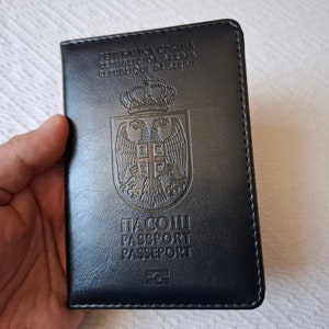 Könnte beinhalten: Ein schwarzer Leder-Reisepass-Schutzumschlag mit dem Text "Republika Srbija, Republic of Serbia, Republique de Serbie" und dem Wappen Serbiens. Der Text "Пасош, Passport, Passeport" ist ebenfalls sichtbar.