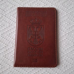 May include: A brown leather passport cover with the text "PASOSUI PASSPORT PASSEPORT" and the coat of arms of Romania.