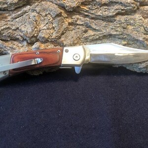 May include: A silver folding knife with a wood handle. The blade is closed and the knife is resting on a piece of bark.