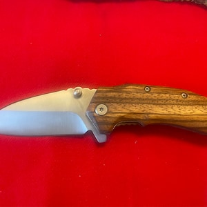 May include: A silver pocket knife with a wood handle. The handle has a dark brown wood grain pattern and is secured with silver screws.