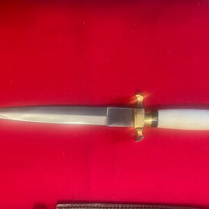 May include: A silver dagger with a white handle and gold accents. The dagger has a sharp point and a double-edged blade.