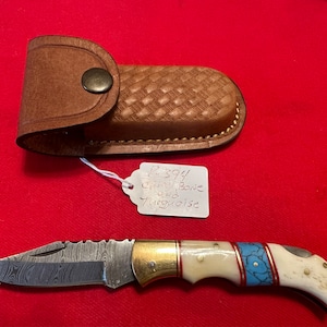 May include: A small pocket knife with a Damascus steel blade, a brass bolster, and a bone handle with turquoise inlay. The knife comes with a brown leather sheath. The tag on the knife reads "P-394  Carved Bone and Turquoise."