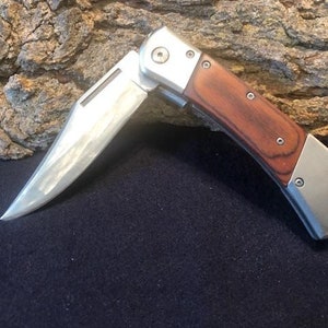 May include: A silver folding pocket knife with a wood handle. The blade is partially open and has a slight curve.