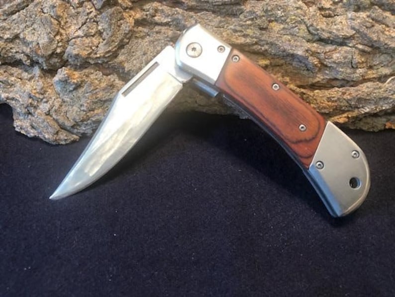 May include: A silver folding pocket knife with a wood handle. The blade is partially open and has a slight curve.