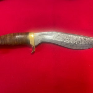May include: A brown leather-handled knife with a brass guard and a silver blade with a patterned finish.