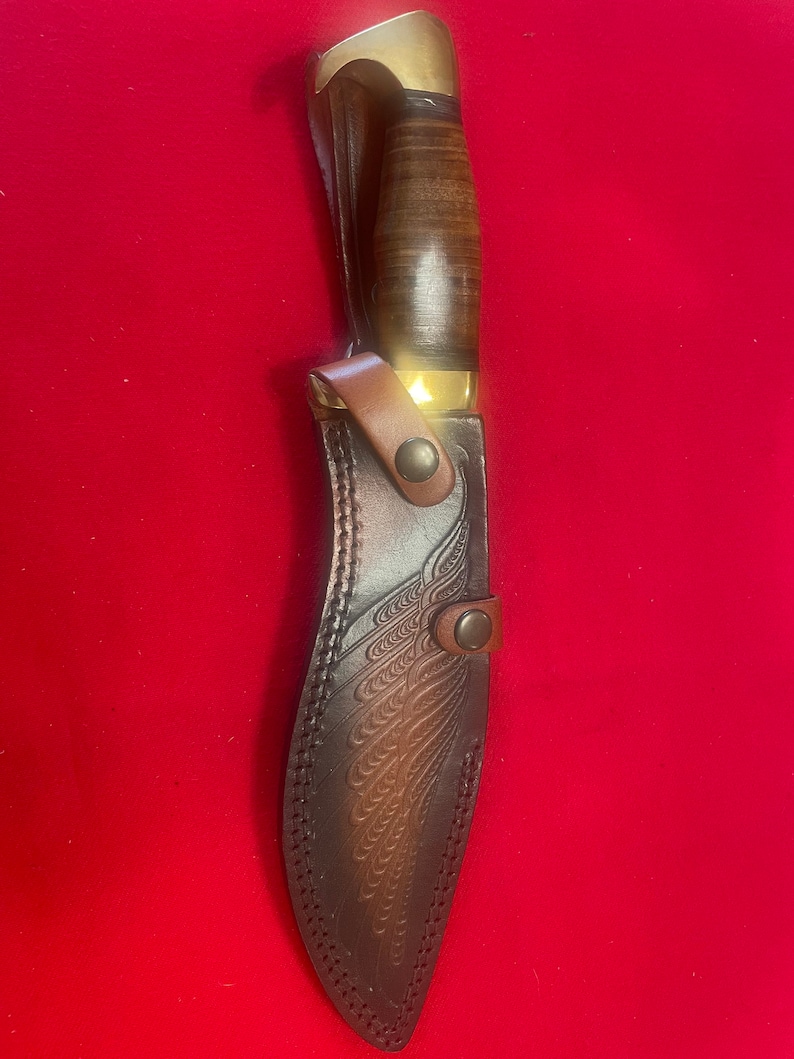 May include: A brown leather knife sheath with a decorative embossed design. The sheath has a brass snap closure and a brass tip.