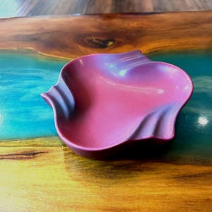 May include: A small, petal-shaped dish in a metallic magenta hue. The dish has a wavy, textured design along the edges, creating a unique and elegant look. The dish is likely made of ceramic or a similar material.