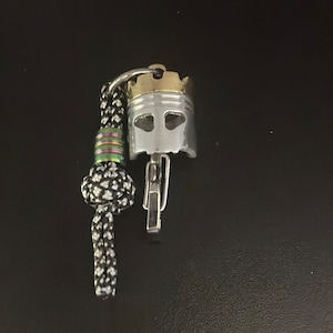 Puede incluir: Un llavero plateado y dorado con una cuerda negra y blanca y un dije en forma de corona plateado y dorado.