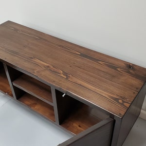 May include: A dark brown wooden media console with two doors and open shelves. The doors are open, revealing the interior shelves. The console has a dark wood finish and is made of solid wood.