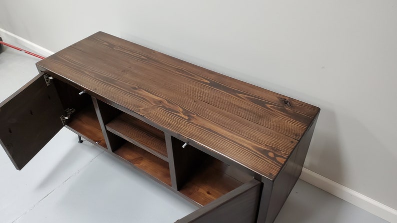 May include: A dark brown wooden media console with two doors and open shelves. The doors are open, revealing the interior shelves. The console has a dark wood finish and is made of solid wood.