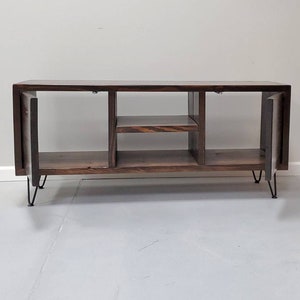 May include: A dark brown wooden media console with two open shelves and two doors. The console has hairpin legs and is sitting on a white floor.