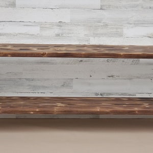 May include: A rustic wooden shelf unit with a dark brown finish. The shelf has a single open shelf and sits on four hairpin legs.
