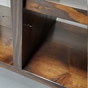 May include: A dark brown wooden shelf unit with multiple shelves. The shelves are made of solid wood and have a natural finish. The unit is designed to be mounted on a wall.