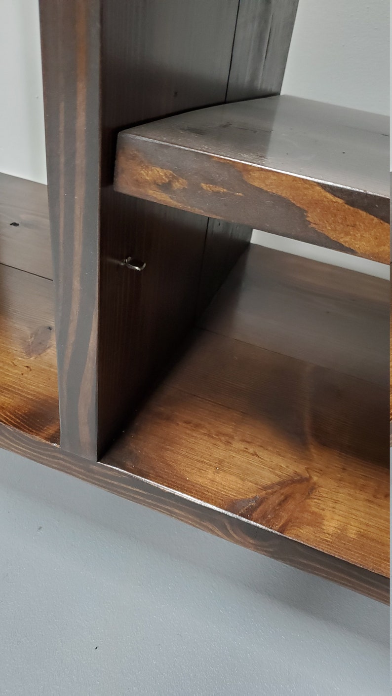 May include: A dark brown wooden shelf unit with multiple shelves. The shelves are made of solid wood and have a natural finish. The unit is designed to be mounted on a wall.