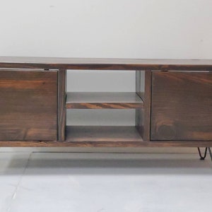 May include: A dark brown wooden media console with two doors and a shelf. The console has hairpin legs.
