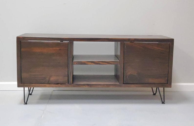 May include: A dark brown wooden media console with two doors and a shelf. The console has hairpin legs.