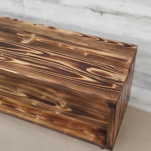May include: A rustic wooden bench with a shelf, featuring a dark brown wood finish with a burnt wood effect.