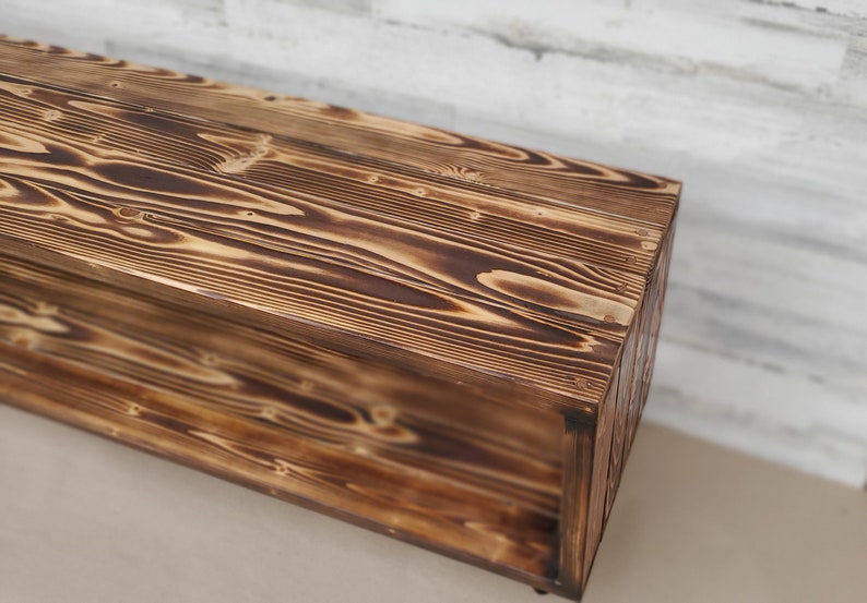 May include: A rustic wooden bench with a shelf, featuring a dark brown wood finish with a burnt wood effect.