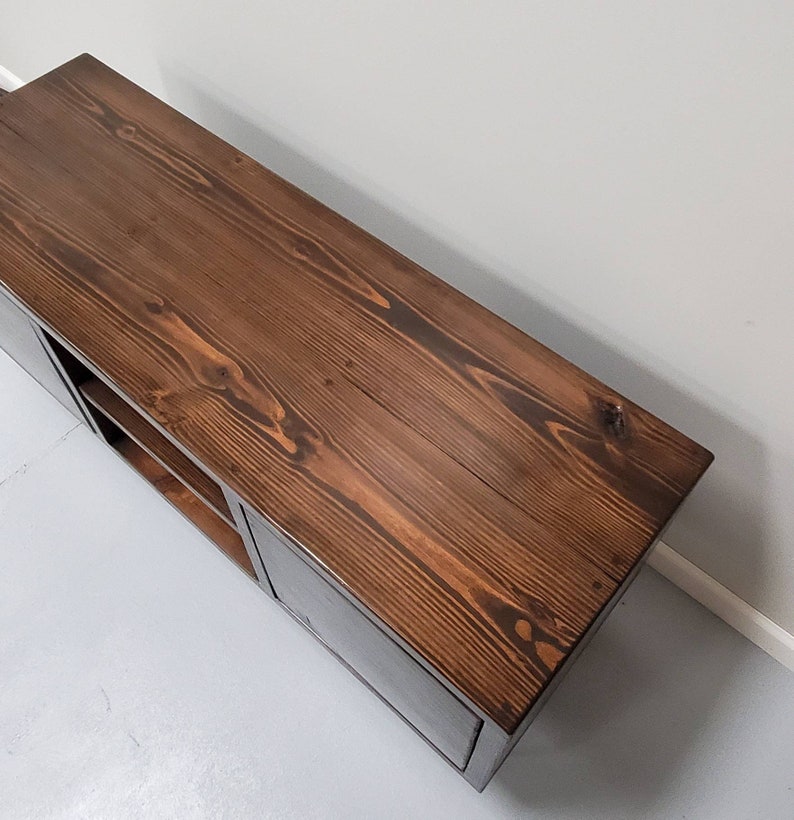 May include: A dark brown wooden media console with two doors and shelves. The console has a distressed wood finish and a rectangular shape.
