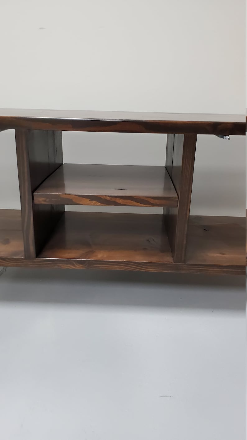 May include: A dark brown wooden entertainment center with two shelves and open compartments. The unit has a simple, modern design.