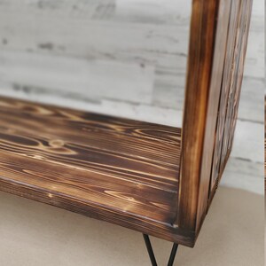 May include: A rustic wooden shelf with a dark brown finish and black hairpin legs. The shelf has a simple rectangular design and is made of reclaimed wood.
