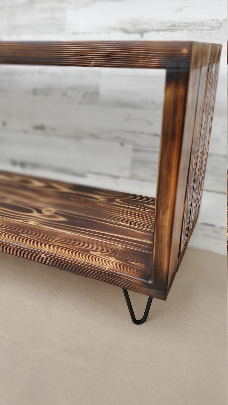 May include: A rustic wooden shelf with a dark brown finish and black hairpin legs. The shelf has a simple rectangular design and is made of reclaimed wood.