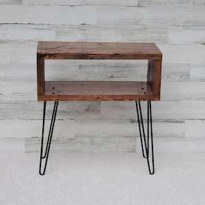 May include: A rustic, wooden side table with a rectangular open design. The table is stained a warm brown and features black hairpin legs. The table is ideal for a living room or bedroom.