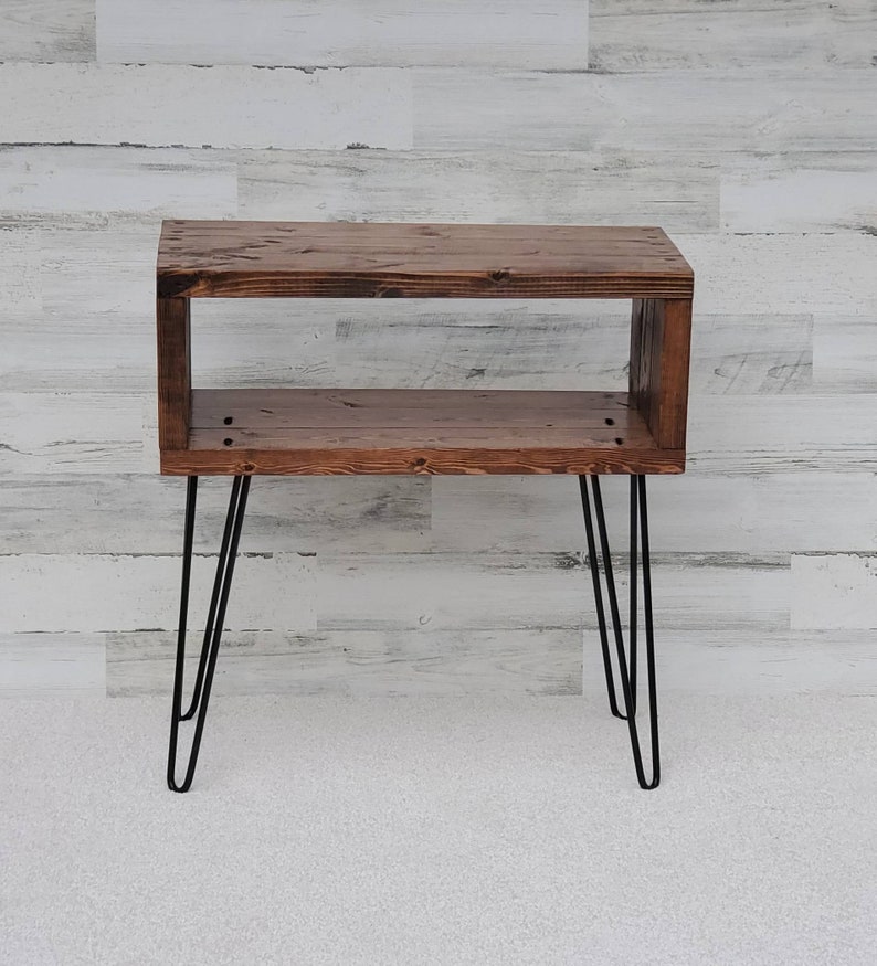May include: A rustic, wooden side table with a rectangular open design. The table is stained a warm brown and features black hairpin legs. The table is ideal for a living room or bedroom.