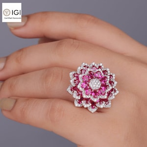 May include: A large, silver ring with a red ruby flower design. The ring is set with many small diamonds and rubies.