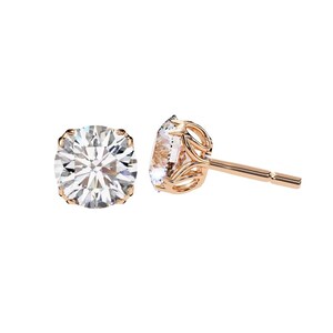 May include: A pair of rose gold stud earrings with a round, clear gemstone. The gemstone is set in a four-prong setting. The earring posts are straight and have a butterfly backing.