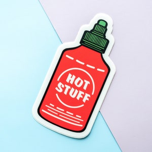 May include: A red and white sticker of a hot sauce bottle with the text "HOT STUFF" in a circle on the label.