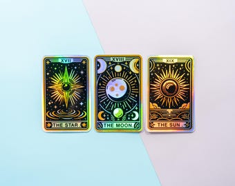 May include: Three holographic tarot cards with gold accents. The cards are numbered XVIII, XIX, and XX. The cards depict The Star, The Moon, and The Sun.