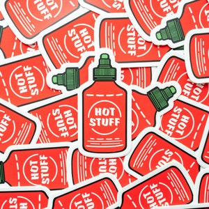 May include: A close-up of several red and white stickers with the text "Hot Stuff" and a cartoon image of a hot sauce bottle. The stickers are arranged in a random pattern.