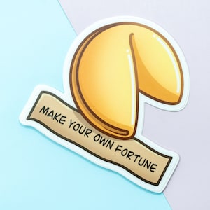 May include: A white sticker with a cartoon illustration of a fortune cookie. The cookie is yellow and has a white outline. The sticker has a banner that says "Make your own fortune".