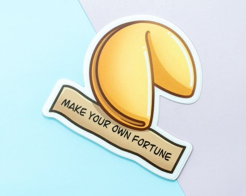 May include: A white sticker with a cartoon illustration of a fortune cookie. The cookie is yellow and has a white outline. The sticker has a banner that says "Make your own fortune".