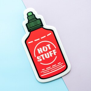 May include: A red and white hot sauce bottle sticker with a green lid and the text "HOT STUFF" in a white circle.