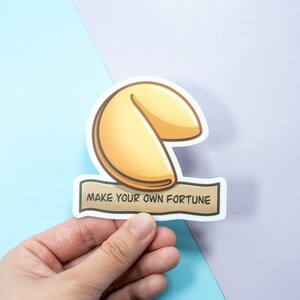 May include: A white sticker with a cartoon illustration of a fortune cookie and the text "Make your own fortune".