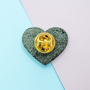 Op de afbeelding: Een zwarte hartvormige emaille-pin met een gouden metalen pin achterkant.