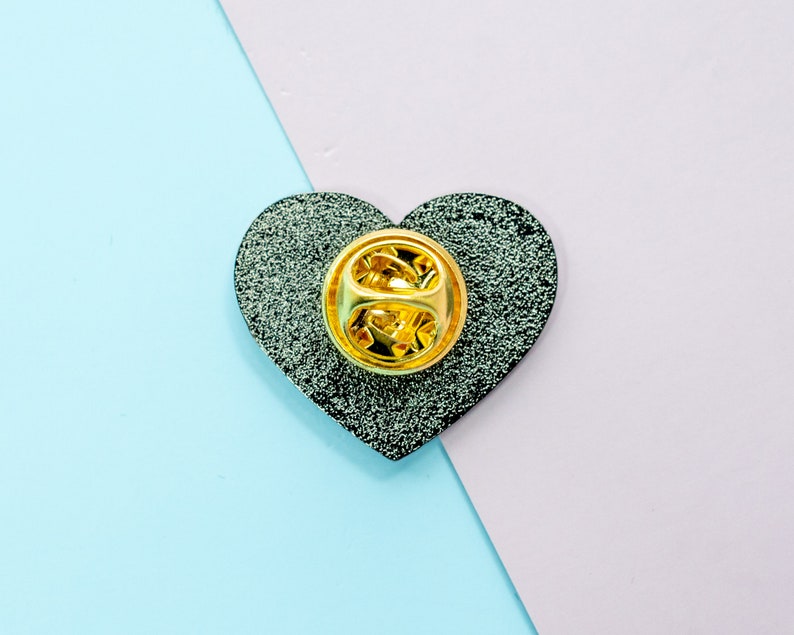 Op de afbeelding: Een zwarte hartvormige emaille-pin met een gouden metalen pin achterkant.