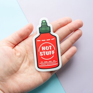 May include: A red and white sticker of a hot sauce bottle with the text "HOT STUFF" in a circle on the label.